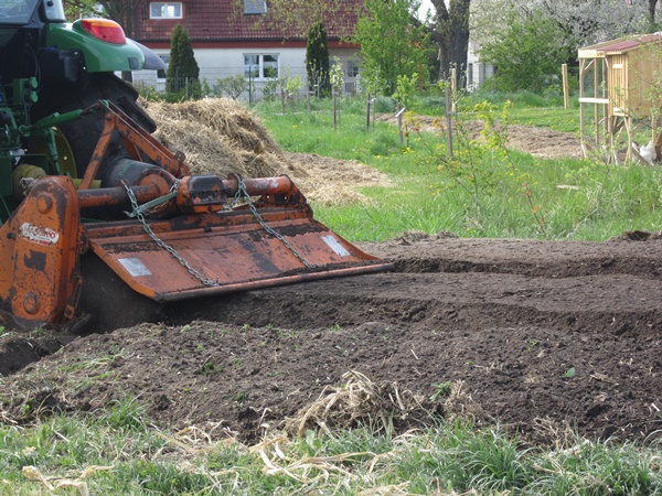 Rotary tiller behind a tractor, tilling a garden bed
