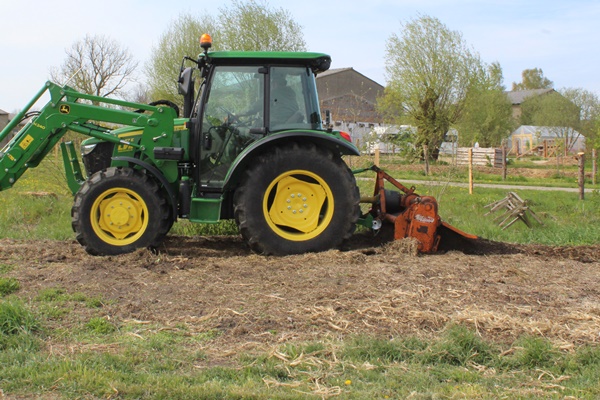John Deere tractor with a rotary tiller, tilling a neglected garden bed