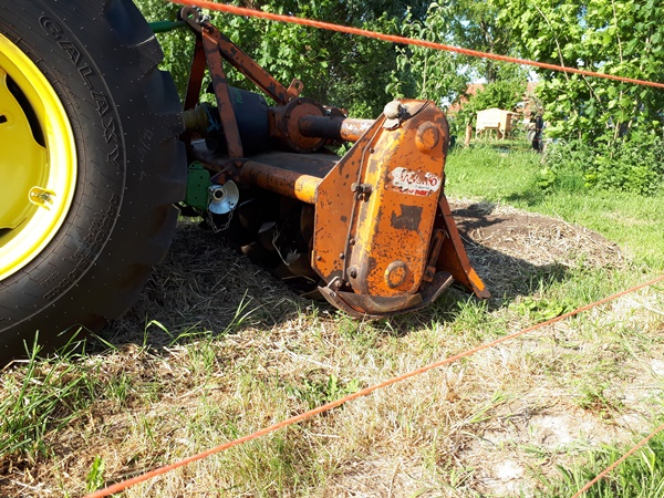 Rotary tiller behind a tractor tilling a garden bed