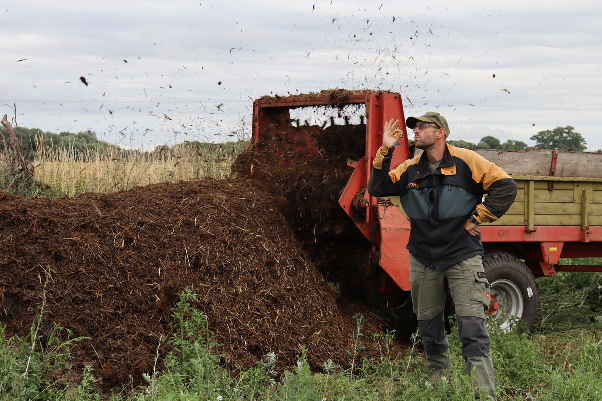 Cow manure being turned of the manure spreader in a big pile on an unused pasture with a man in frond with a happy expression
