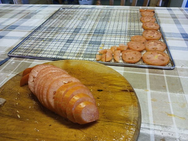 Wooden cutting board with tomato slices and a rack from a dehydrator with tomato slices, lying on a table